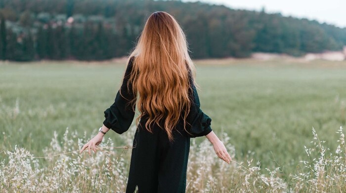 woman in black dress in a green field with her red hair down photographed from behind