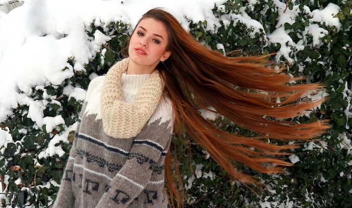 woman in a large grey and white sweater with her long red hair in front of a tree covered in snow