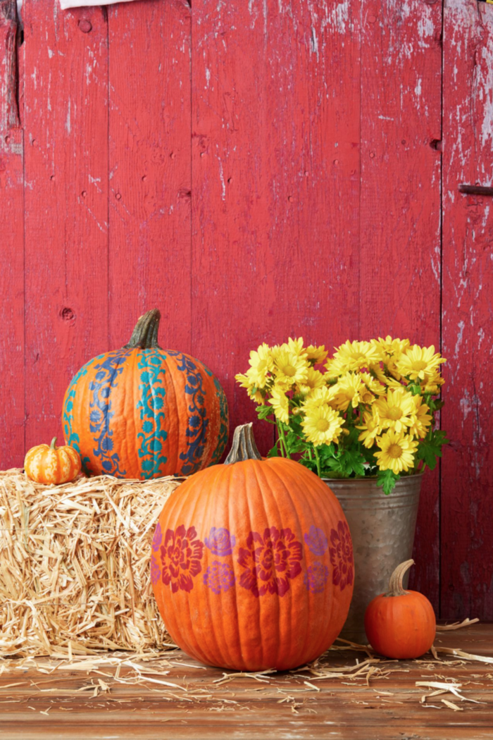 outdoor decor with hay painted pumpkins yellow flowers in a bucket on a red wall