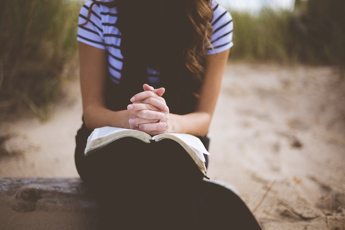 woman with long hair sitting on the beach with a book in her lap praying