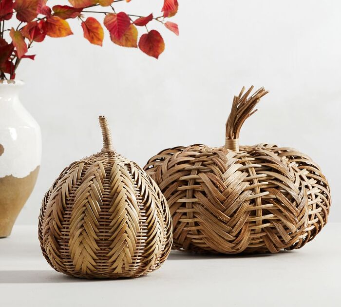 two woven pumpkins on a white table with a vase with foliage next to them