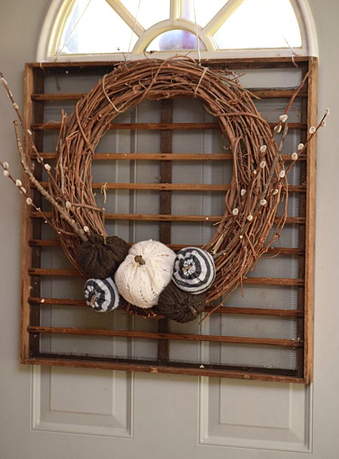 sweater pumpkin wreath made of dry branches hanging on the inside of a white door