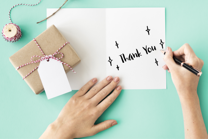 woman writing a thank you note on a light blue background
