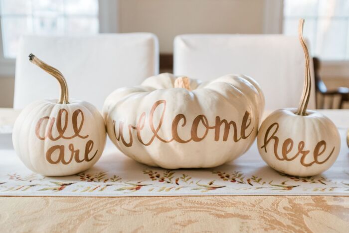 three white pumpkins with golden words on them on a table saying all are welcome here