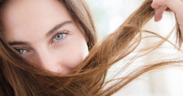 woman with light skin and blue eyes holding a strand of hair in front of her face