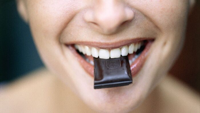 woman biting a piece of dark chocolate between her teeth and lips