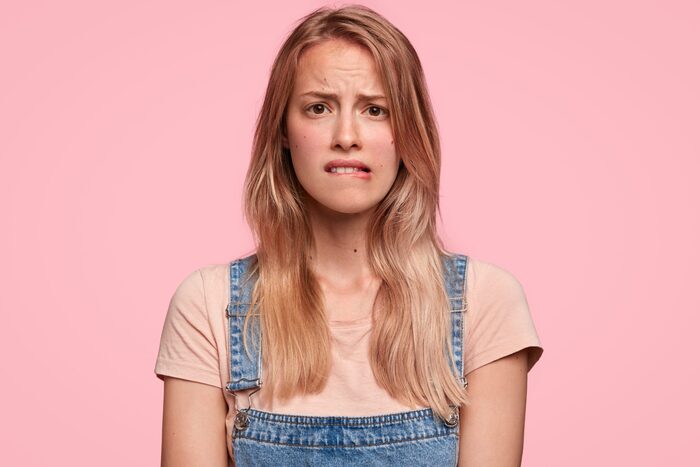 seasonal hair loss woman on a pink background with blond hair looking worries and biting her lip