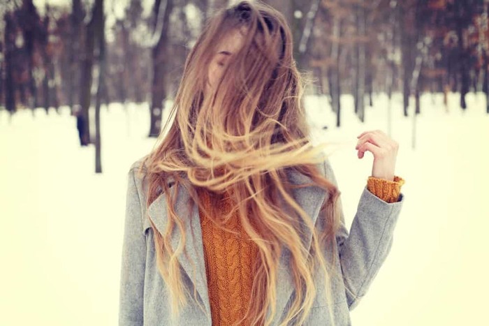 woman dressed in a sweater and grey coat posing outdoors in the snow with her long blond hair down in front of her face