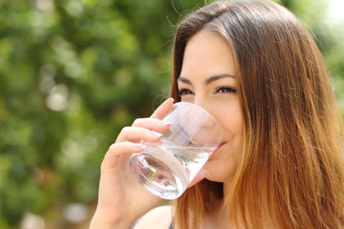 woman with brown hair drinking from a glass of water outdoors