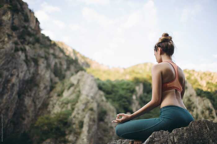 woman dressed in sportswear sitting on a rock outside in nature meditating