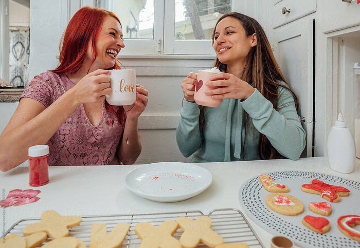 women drinking hot cocoa at home eating cookies and laughing together