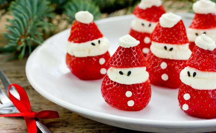 Healthy Christmas desserts strawberyy santas on a while plate with pine branches in the background