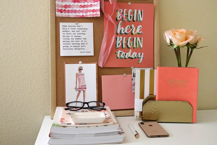 small pink themes vision board standing on a desk against a wall with roses and stationary around it