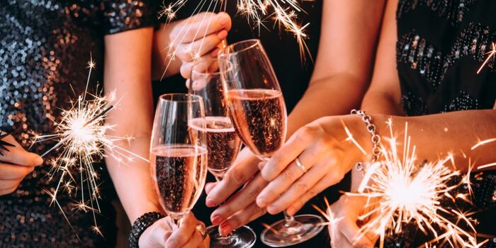 womens' hands holding elegant champagne glasses filled with pink sparkling wine holding sparklers