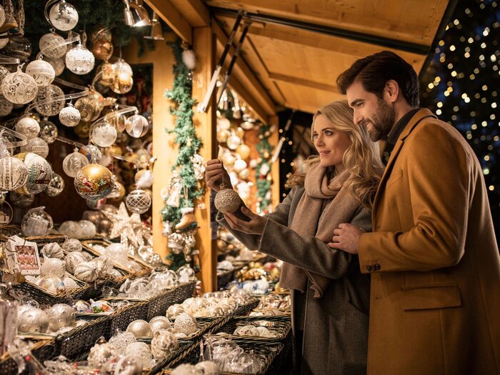 couple enjoying a christmas market in vienna in front of a christmas pavillion choosing holiday decorations