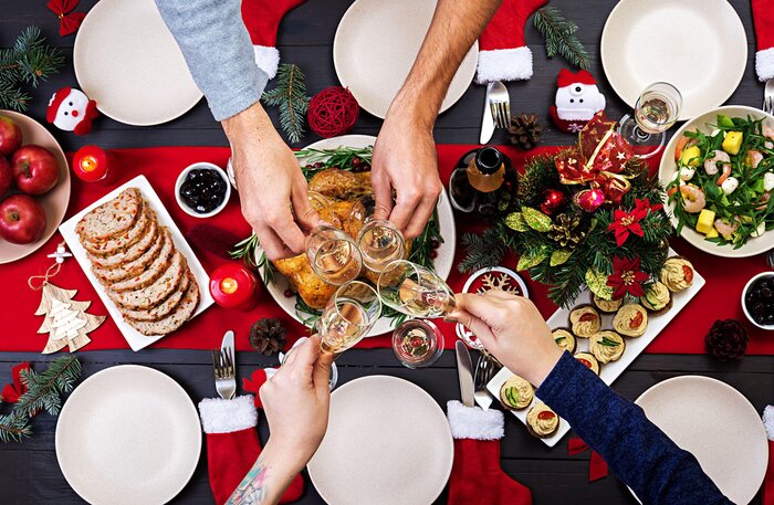 hands holding wine glasses cheering with a toast over a christmas table with various special meals on a red cloth