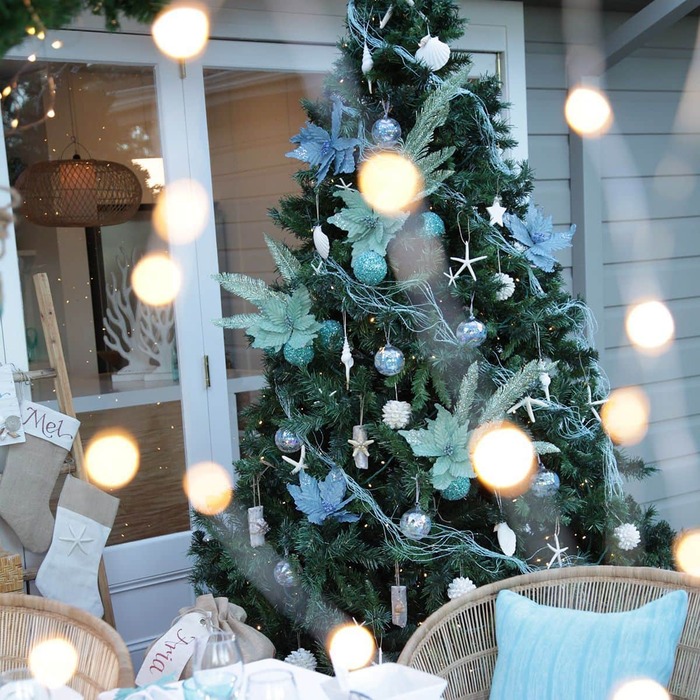 coastal blue holiday team outdoor christmas tree with light blue decorations and fairy lights on the window