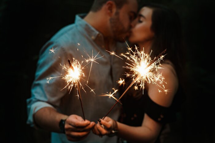 couple kissing in a dark space holding sparklers in their hands