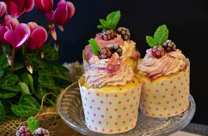 three cupcakes on a plate with fruits on top and flowers around