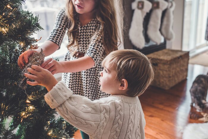 two young children decorating a christmas tree at home with a home environment in the background