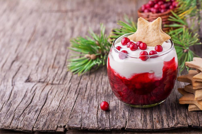 Christmas dessert on a wooden table with red berries a cookie and white whipped cream