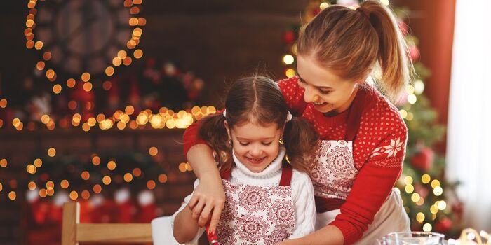 family baking woman and daughter baking in christmas clothes with lights and decorations in the background