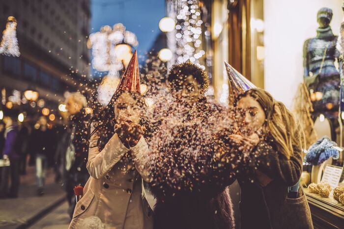 friends celebrating new years eve outdoors with party hats on and blowing confetti