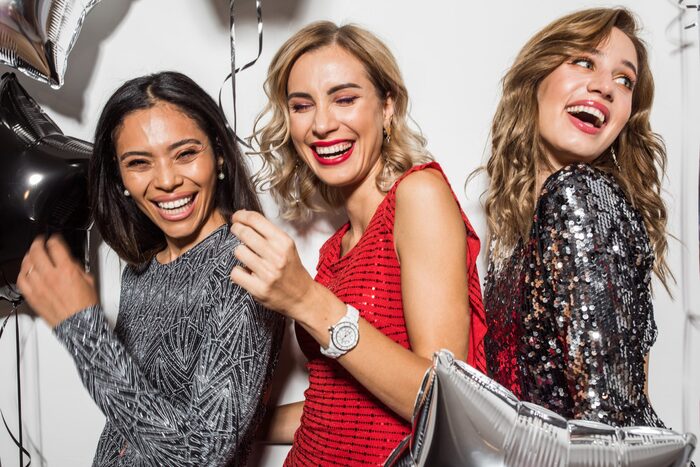 three girlfriends in sparkly dresses celebrating new year surrounded by balloons