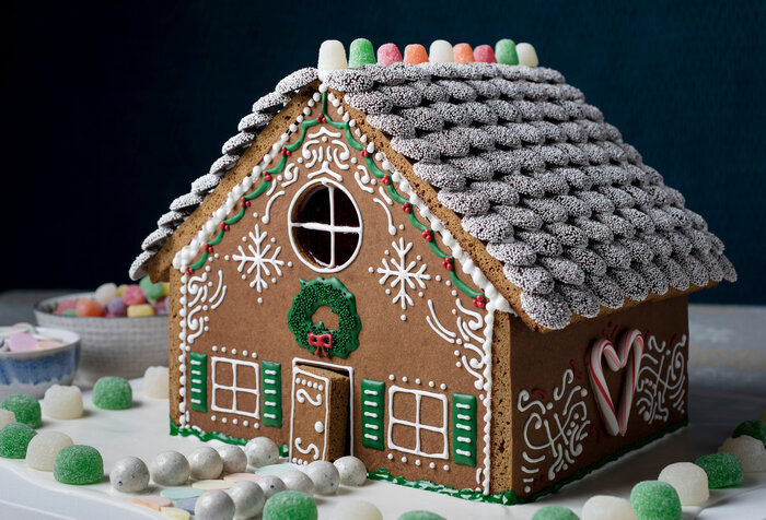 traditional gingerbread house with gummies and sugar snow on the roof on a black background