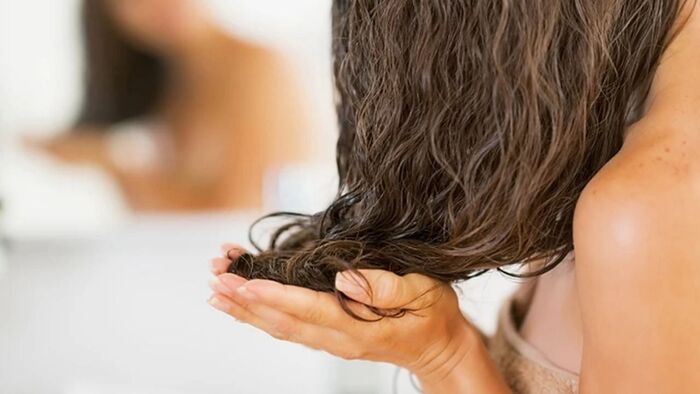 close up woman applying oils to her wet hair with her hands