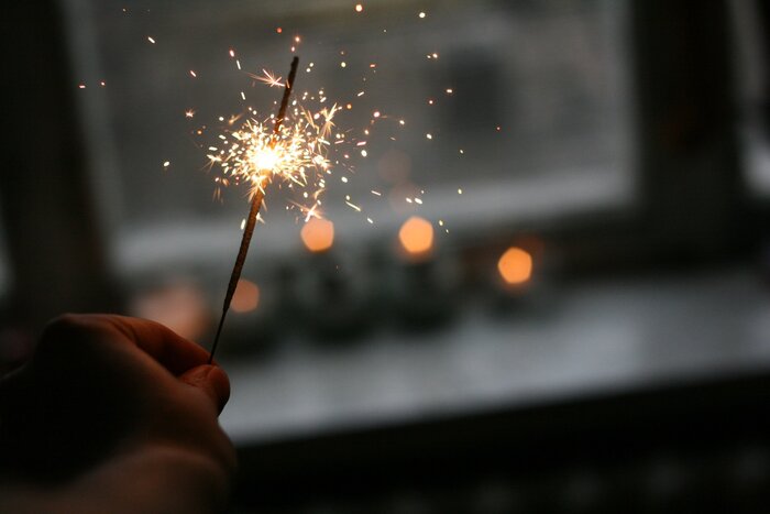 hand holding a sparkler in a dark room against a window