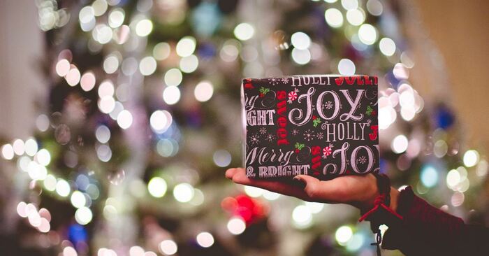 a hand holding a present with black wrapping with the word holly and joy on it christmas tree on the background