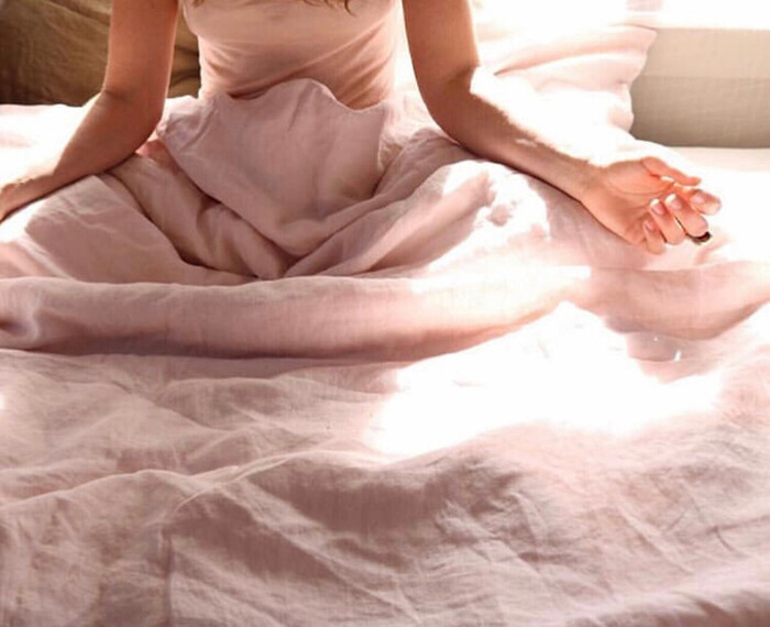 woman waking up meditating in bed with sunlight in the background