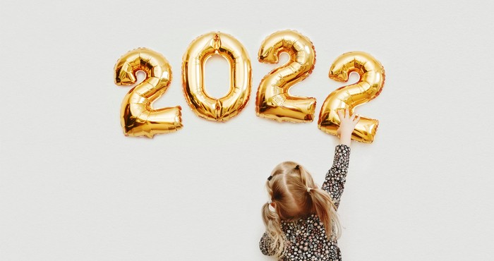 Little girl decorates the wall of the house with golden numbers 2022. Preparing the house for Christmas and New Year.