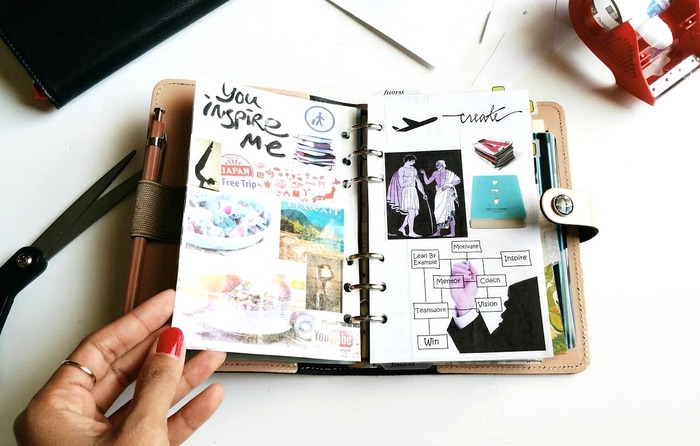 woman's hand going through a notebook with inspirational images on a white desk