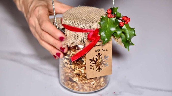 hand holding a decorated jar with burlap and red ribbon filled with walnuts
