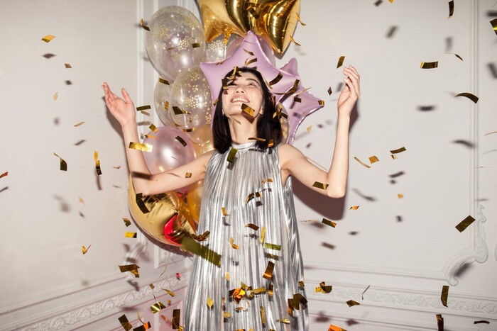 woman in a silver dress in a white room with balloons and golden confetti flying in the air