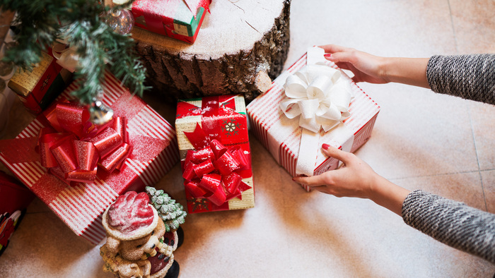 Close up of woman hands putting down a gift box under a Christmas tree with other beautifully wrapped gifts around