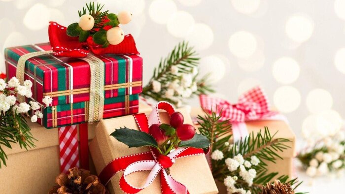 a pile of christmas presents wrapped in colorful wrapping with pine branches and berries decor