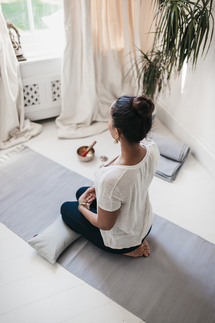 woman sitting in a meditative pose setting intentions in a light room on a gray yoga mat