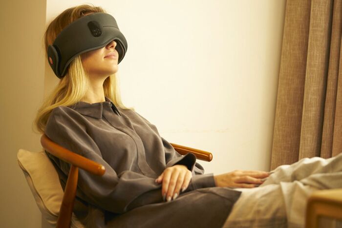 woman with long blond hair sitting in a chair with a modern sleeping mask on relaxing