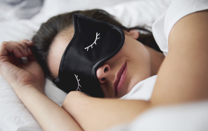 Portrait of young woman in bed with a black sleeping mask on enjoying her sleep