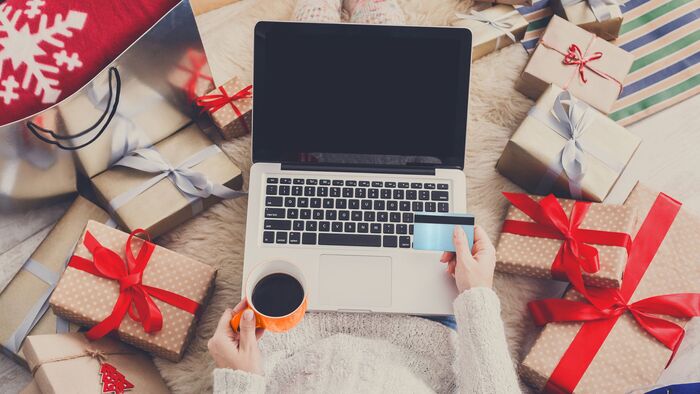 woman in a pullover sitting with a laptop credit card and coffee cup in her hands surrounded by beautifully wrapped gifts