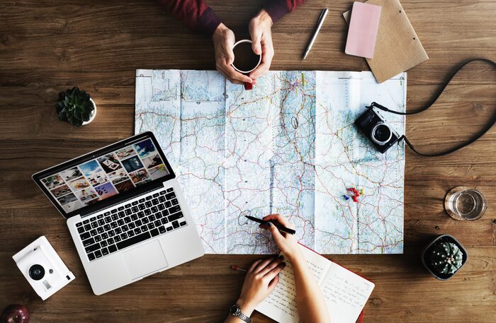 couple sitting on the two sides of a table with a map on it a laptop and a photo camera doing planning