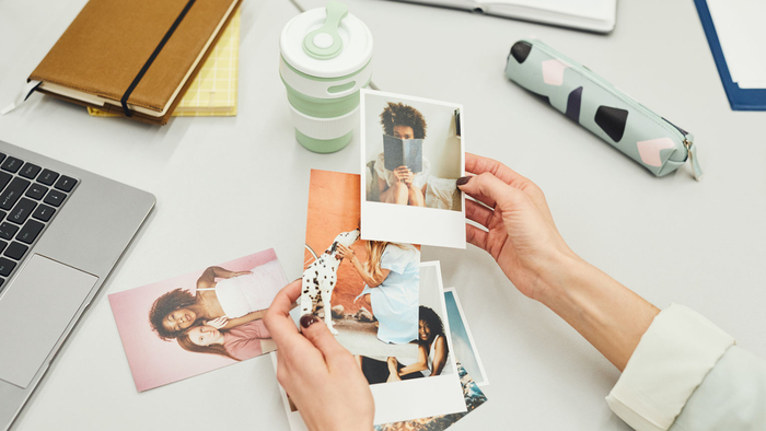 hands holding different photos on a white desk with stationary scattered around