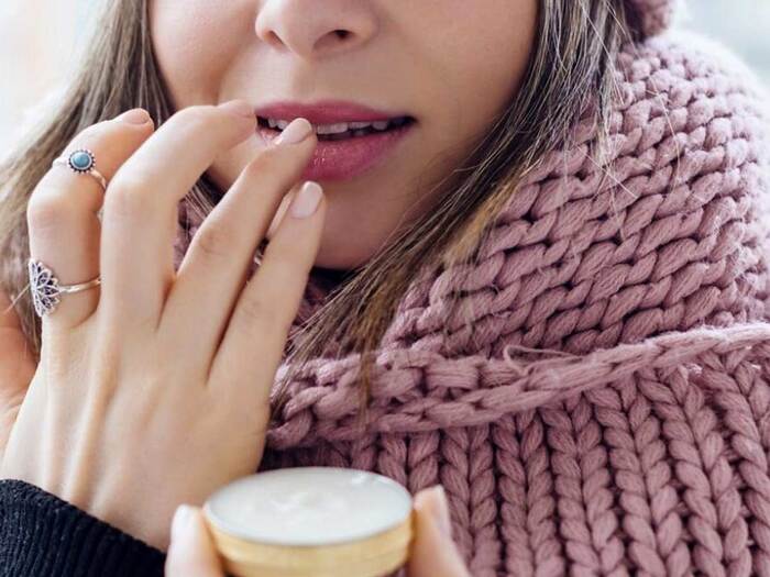 winter skin care woman in a large pink scarf close up applying lip balm on her lips