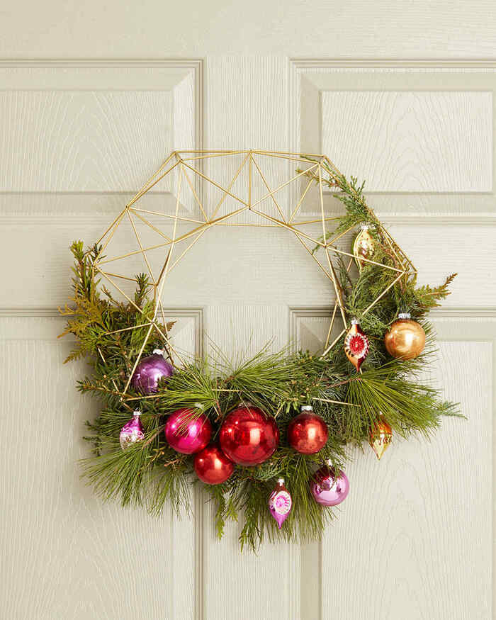 winter holiday wreath on white door golden metal and asymmetrical decoration with green foliage and colorful baubles