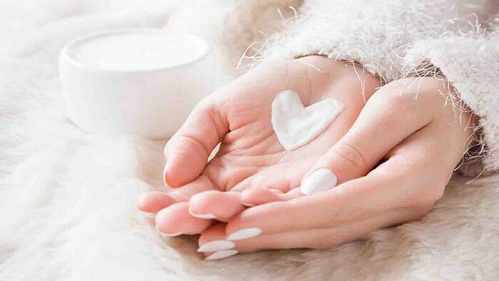 hands of a woman close up on a white background with white cream and a heart on her palms