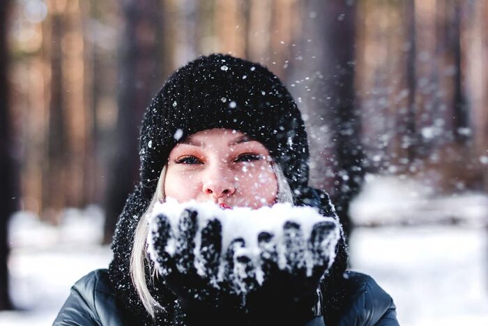 woman dressed in black outdoors blowing on a handful of snow