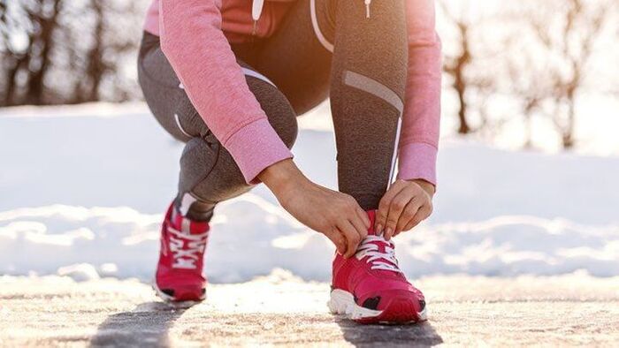 winter sport woman dressed in sportswear outside in the snow fixing her shoe